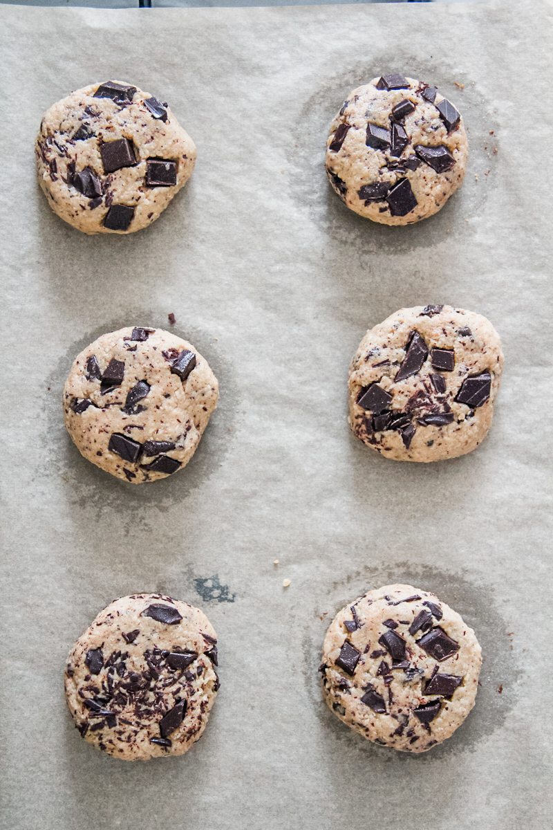 Unbaked tahini chocolate chunk cookies sit on a lined baking tray.