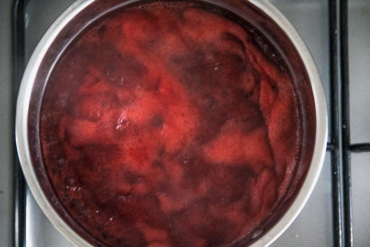 Roasted strawberry sauce sits in a stainless steel pot on the stovetop.