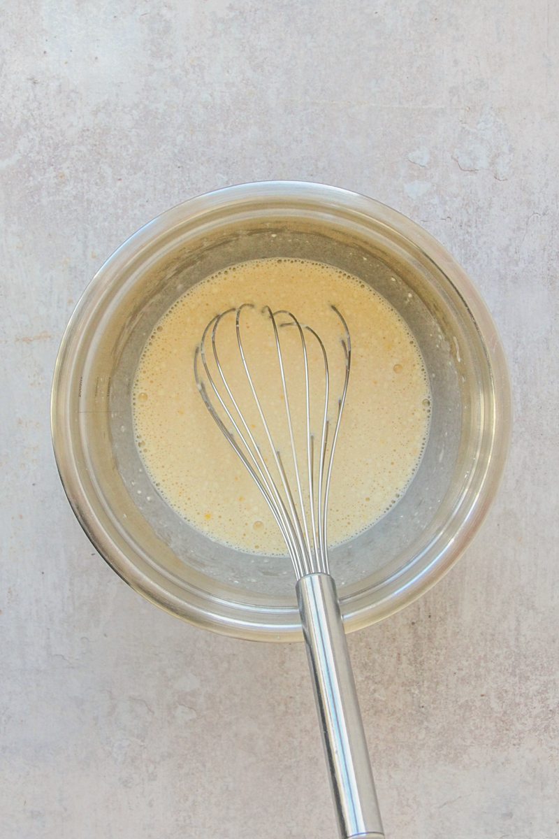 A custard mixture sits in a stainless steel bowl on a gray surface.