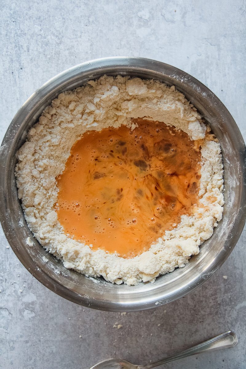 Beaten eggs sit in a well of floir and butter in a stainless steel bowl on a gray surface.