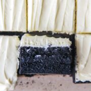 A close up of a black cocoa brownie with white chocolate frosting sits on it's side.