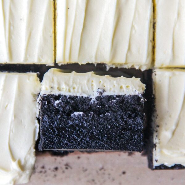 A close up of a black cocoa brownie with white chocolate frosting sits on it's side.