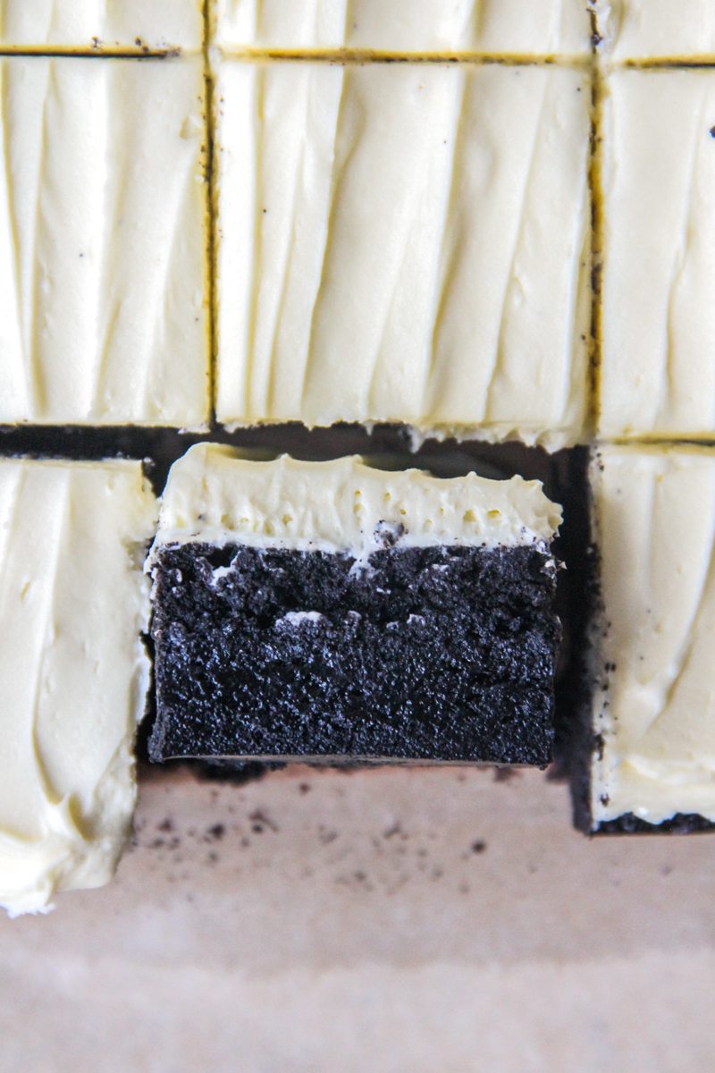 A close up of a black cocoa brownie with white chocolate frosting sits on it's side.