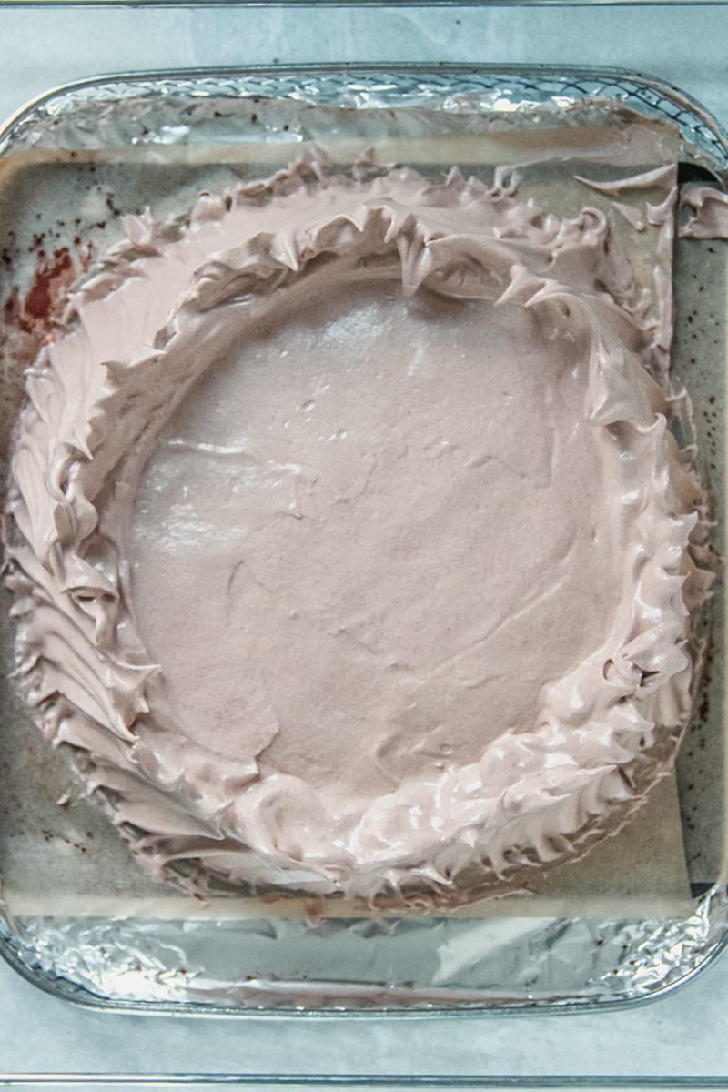 Unbaked chocolate pavlova sits on a lined baking tray on a gray surface.