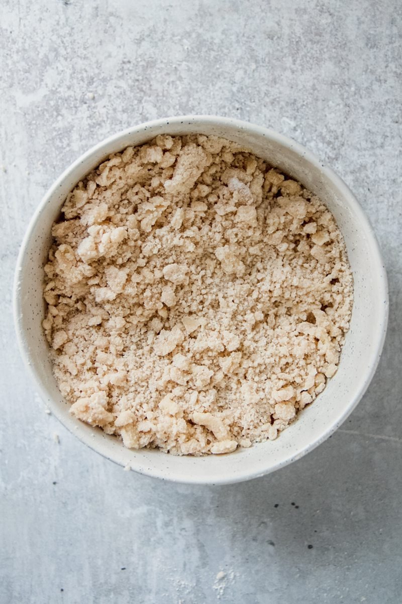 A streusel mixture sits in a white ceramic bowl on a gray surface.