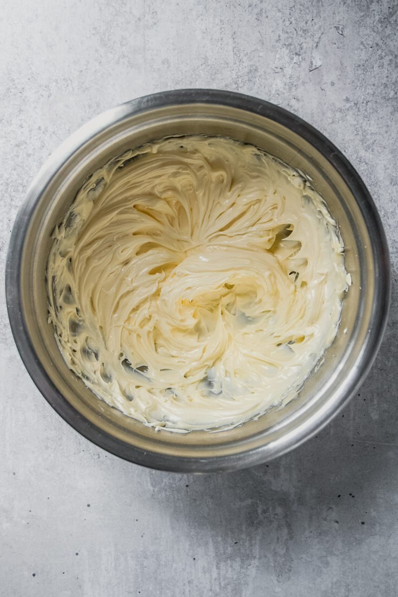 Whipped butter and sugar sits in a stainless steel bowl on a gray surface.