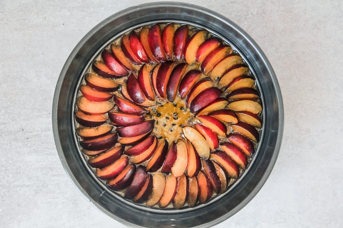 Sliced plums sit on top of a passionfruit syrup in a cake tin for an upside down plum cake