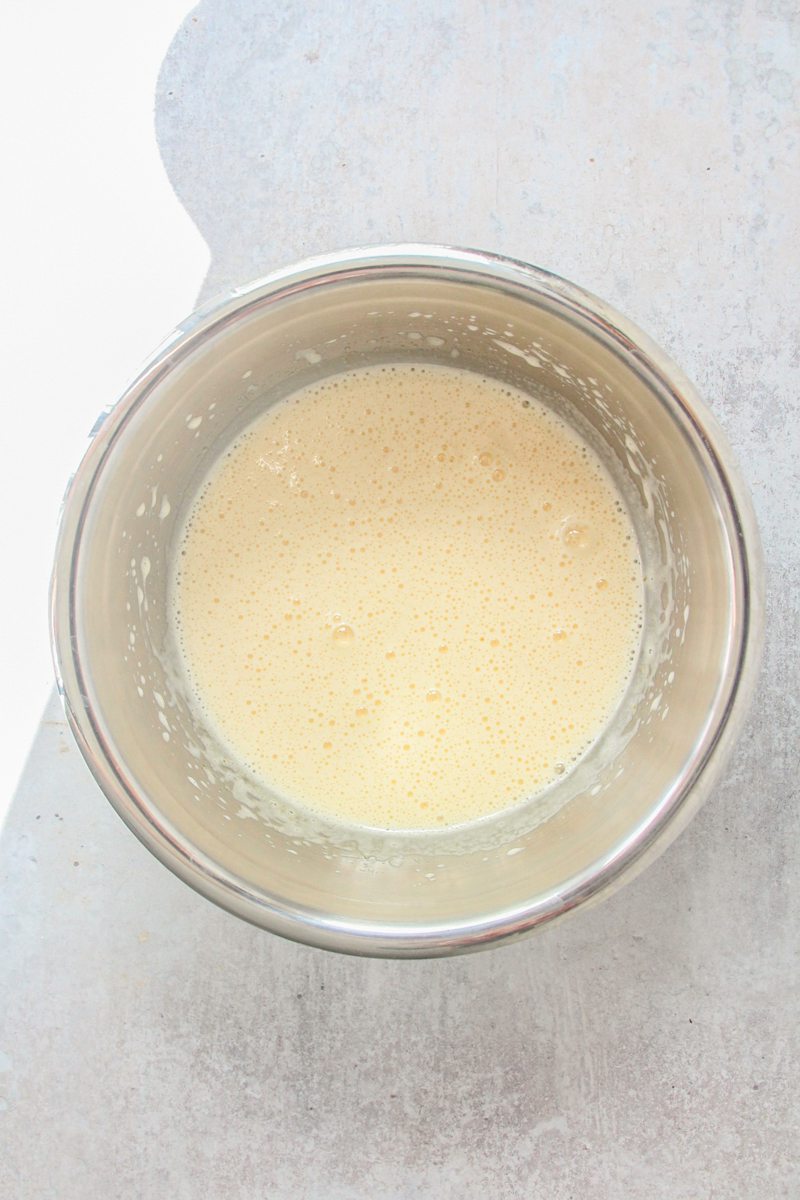 A wet base for a cake sits in a stainless steel bowl on a gray surface.