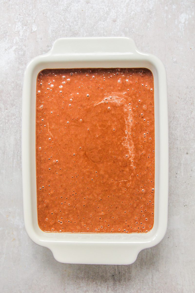 Unbaked chocolate cake batter sits in a rectangle white ceramic dish on a gray surface.