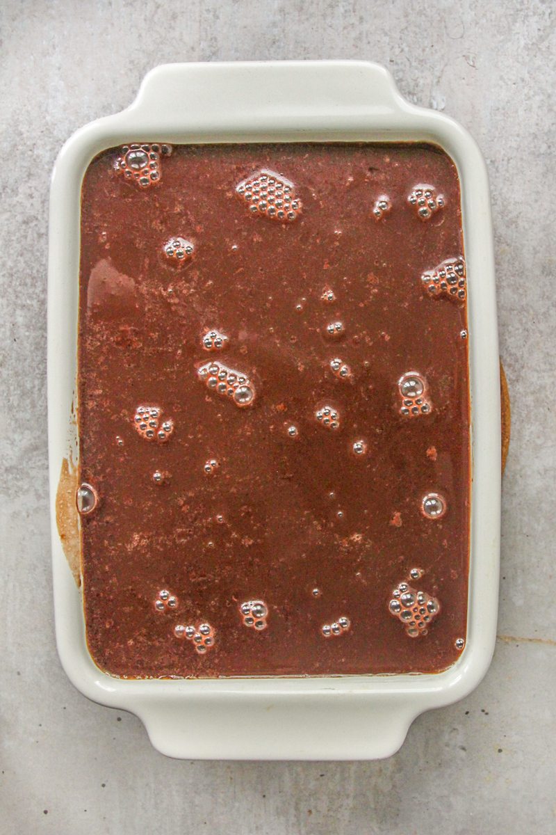 Chocolate sauce on top of a cake in a rectangle white ceramic dish on a gray surface.