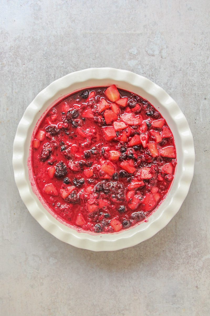 Apples and berries sit in a round white ceramic bowl on a gray surface.