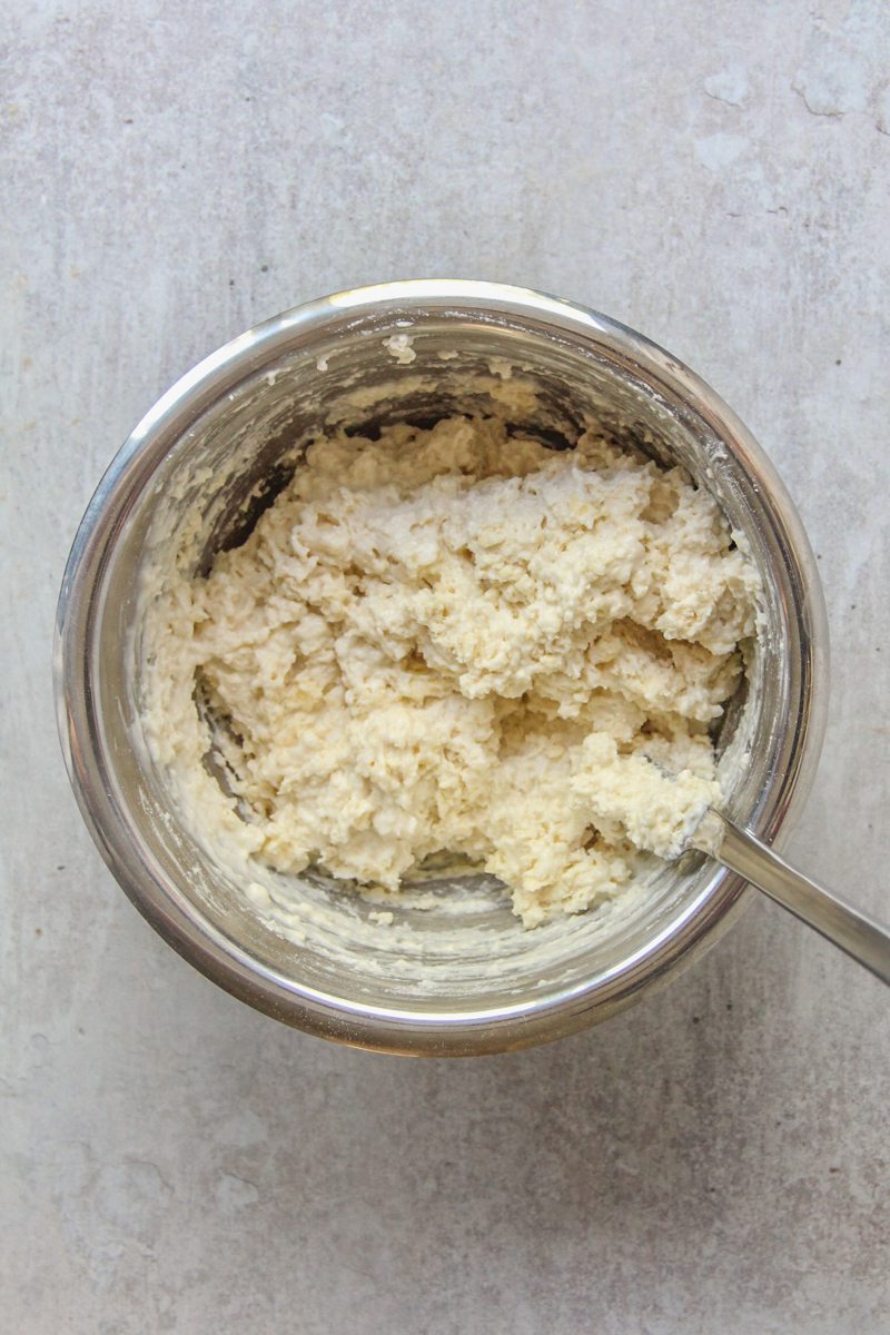 Cobbler dough sits in a stainless steel bowl on a gray surface.