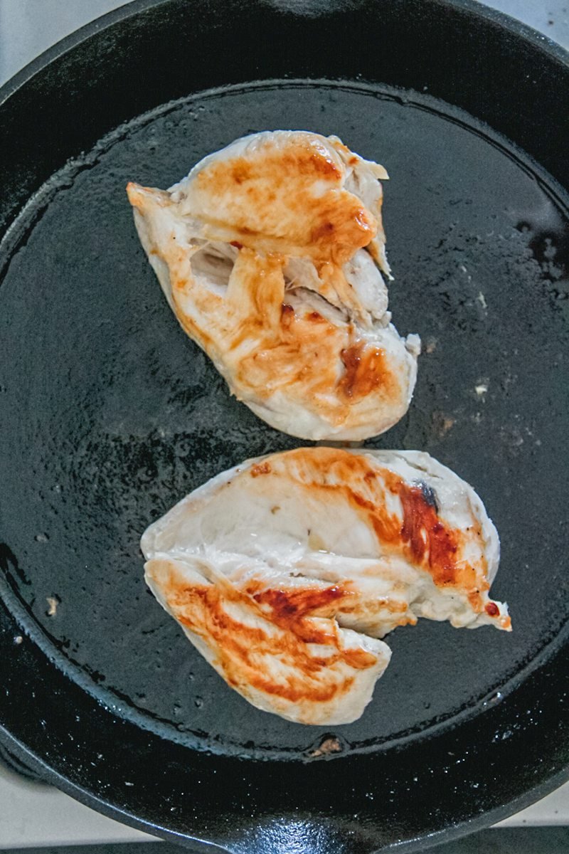 Golden chicken breasts sit in a cast iron skillet on a cooker.