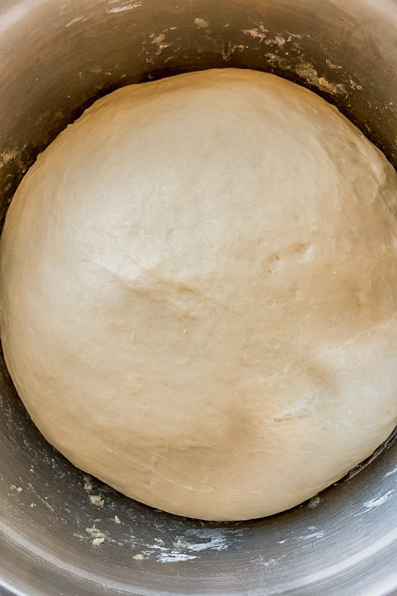 Risen dough sits in a stainless steel bowl.