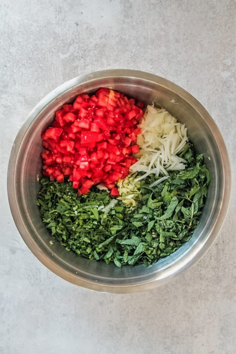 Chopped vegetables in a stainless steel bowl on a gray surface.