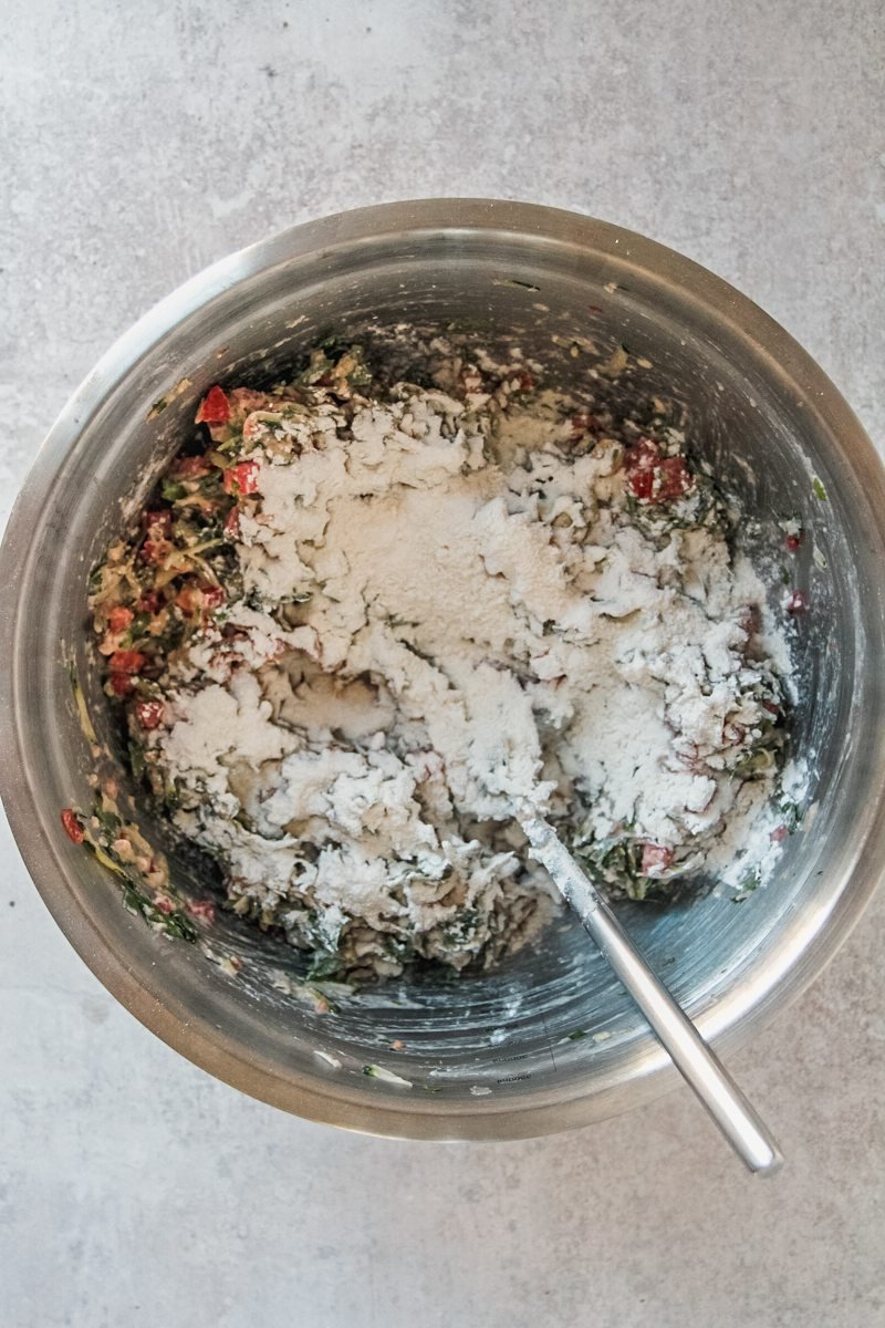 Dry ingredients sit on top of chopped vegetables in a stainless steel bowl on a gray surface.