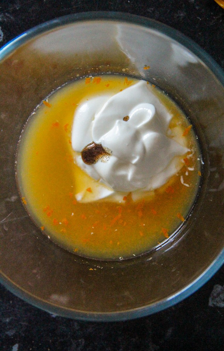 Orange juice, Greek yogurt and vanilla paste sits in a glass beaker on a dark surface.