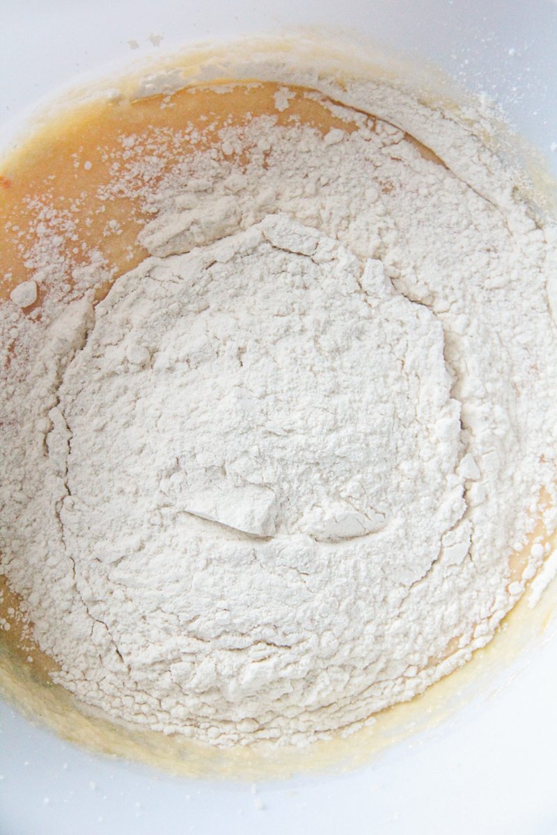 Dry ingredients sit on top of whipped wet cake ingredients in a white bowl.