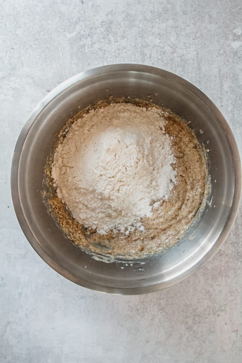 Dry ingredients sit on top of cake batter in a stainless steel bowl on a gray surface.