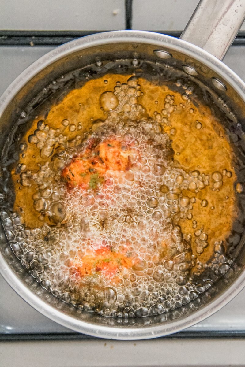 A tomato fritter is fried in a saucepan filled with oil on a cooker.