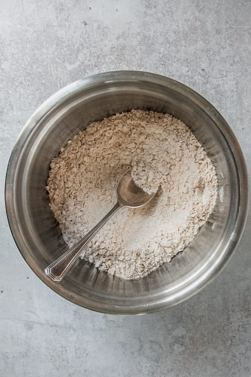 A crumb mixture sits in a stainless steel bowl on a gray surface.