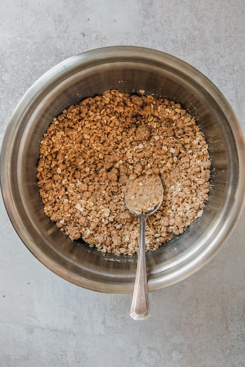 A streusel mixture sits in a stainless steel bowl on a gray surface.