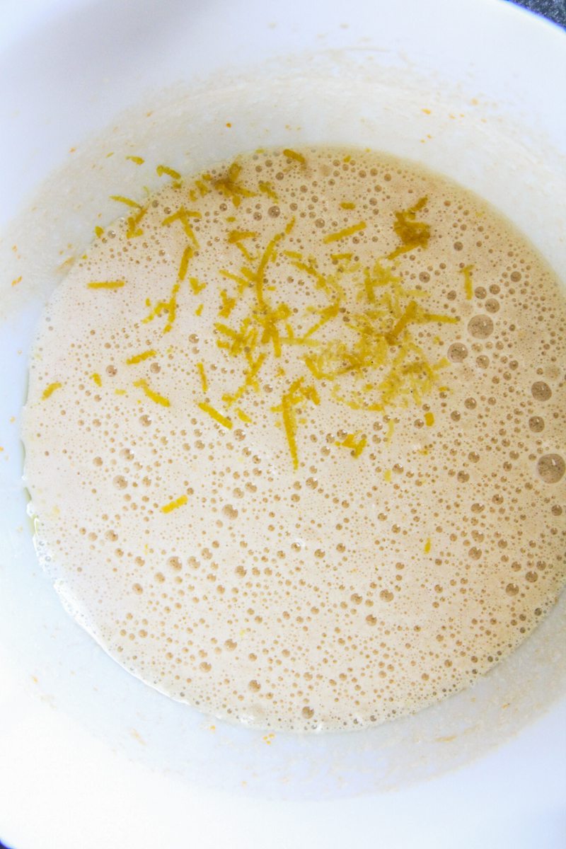 Lemon zest sits on top of whipped sugar and eggs in a white bowl.