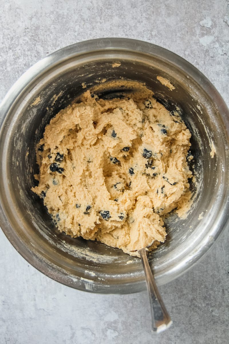 A blueberry muffin cookie dough sits in a stainless steel bowl on a gray surface.