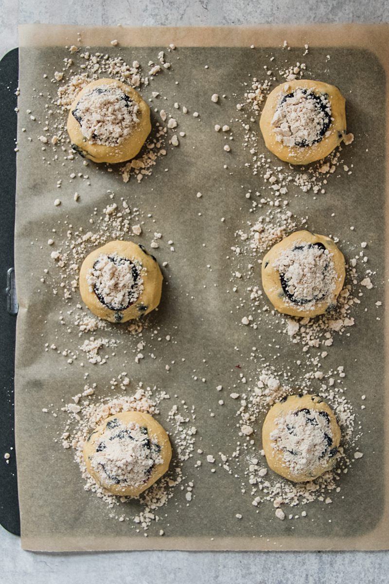 Unbaked blueberry muffin cookies sit on a parchment paper lined baking tray on a gray surface.