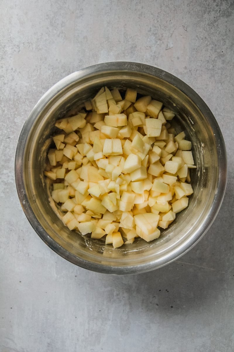 Finely cubed apples sit in a stainless steel bowl on a light gray surface.