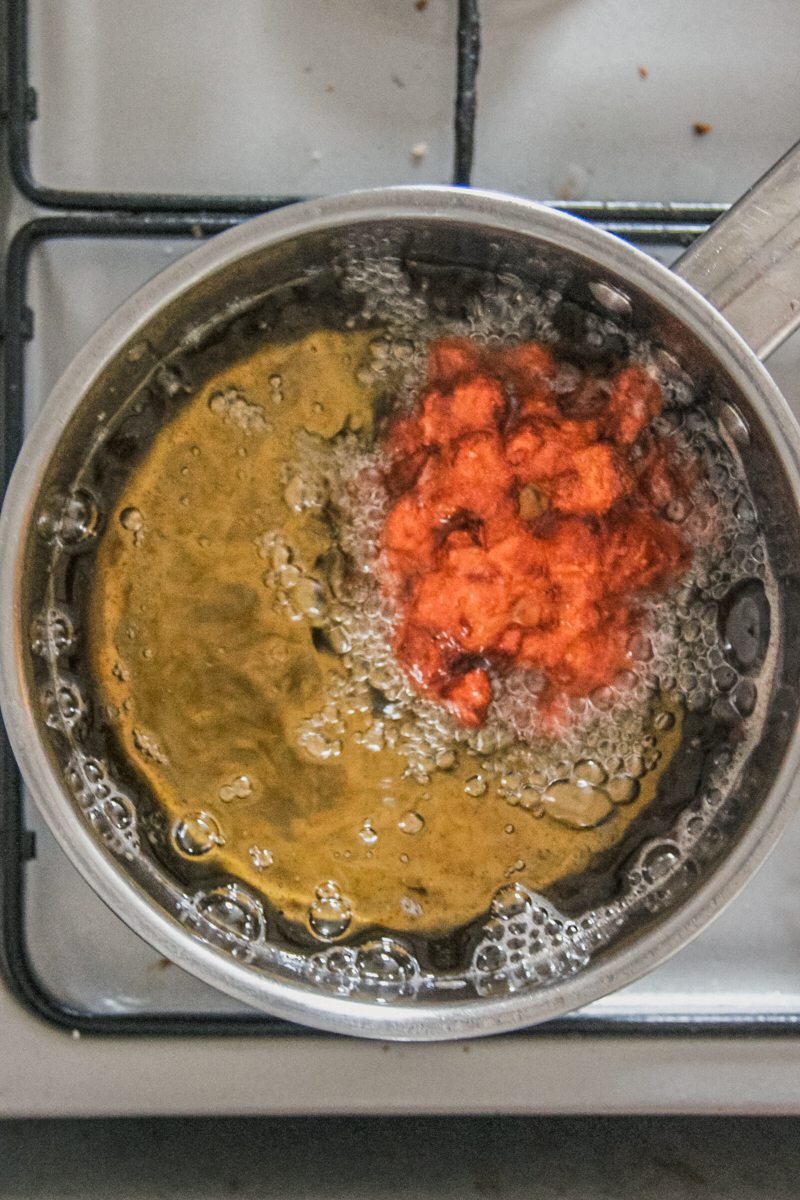 An apple fritter is cooked in hot oil in a saucepan on a cooker.