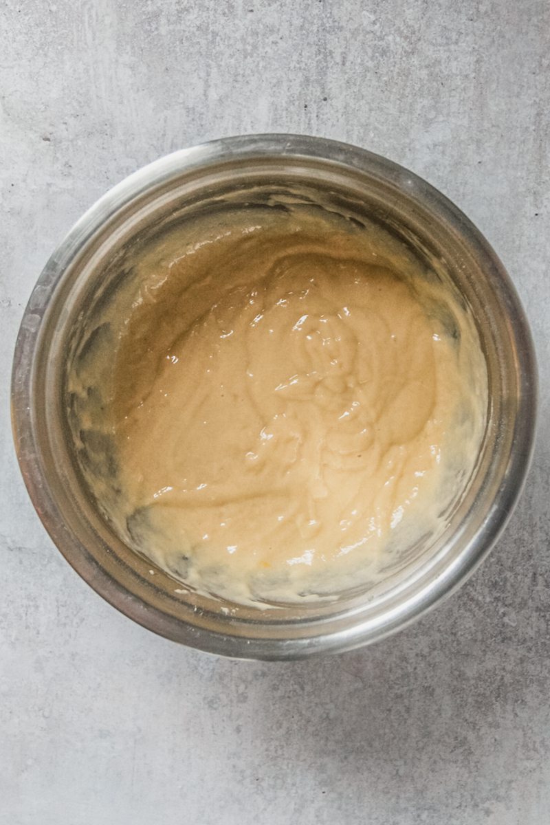 Griddle cake batter sits in a stainless steel bowl on a gray surface.