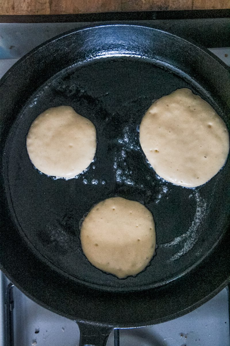 Griddle cakes cook in a cast iron skillet on a cooker.