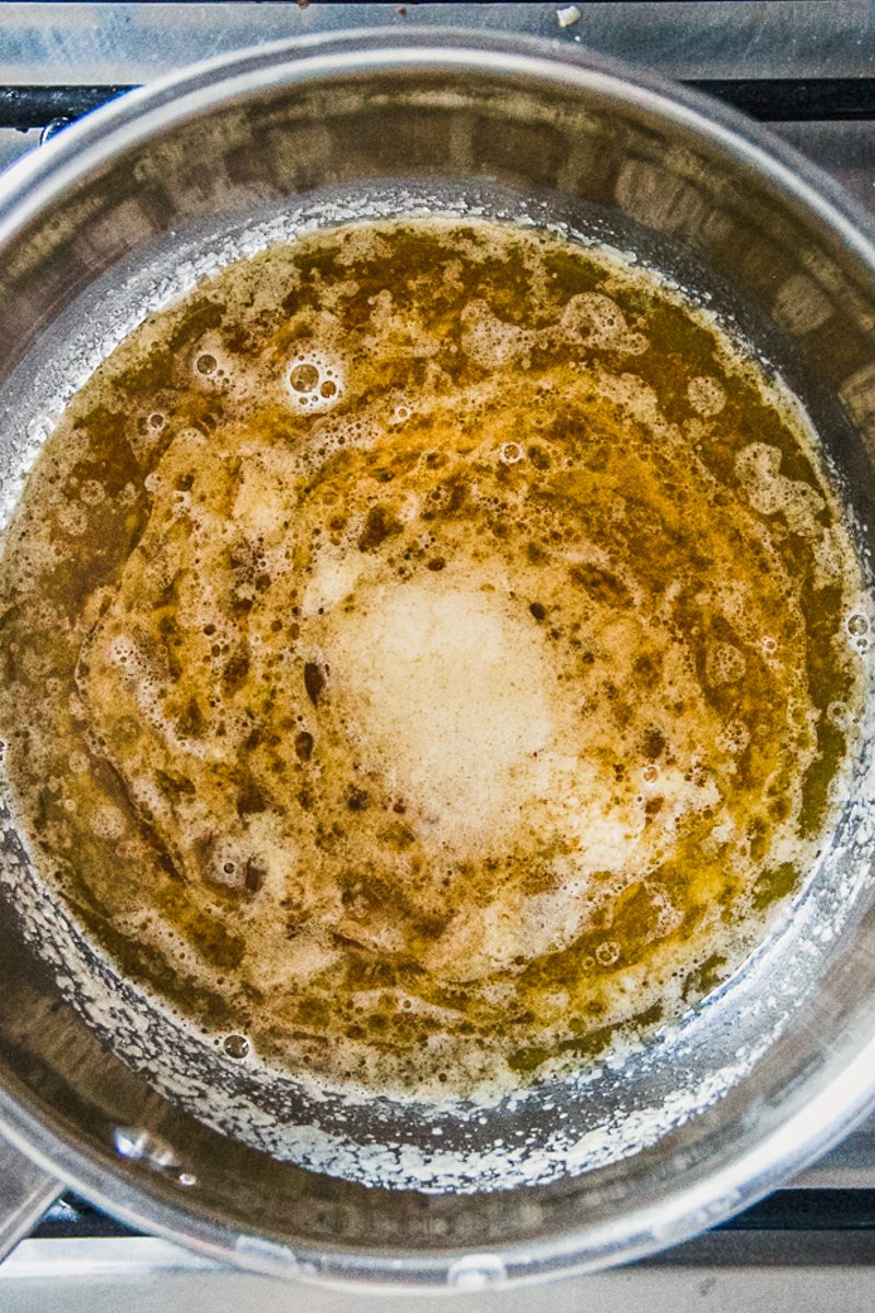 Melted butter with a bloom of baking soda sits in a stainless steel saucepan on a cooker.