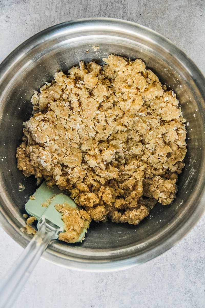 Anzac biscuit mixture sits in a stainless steel bowl on a gray surface.