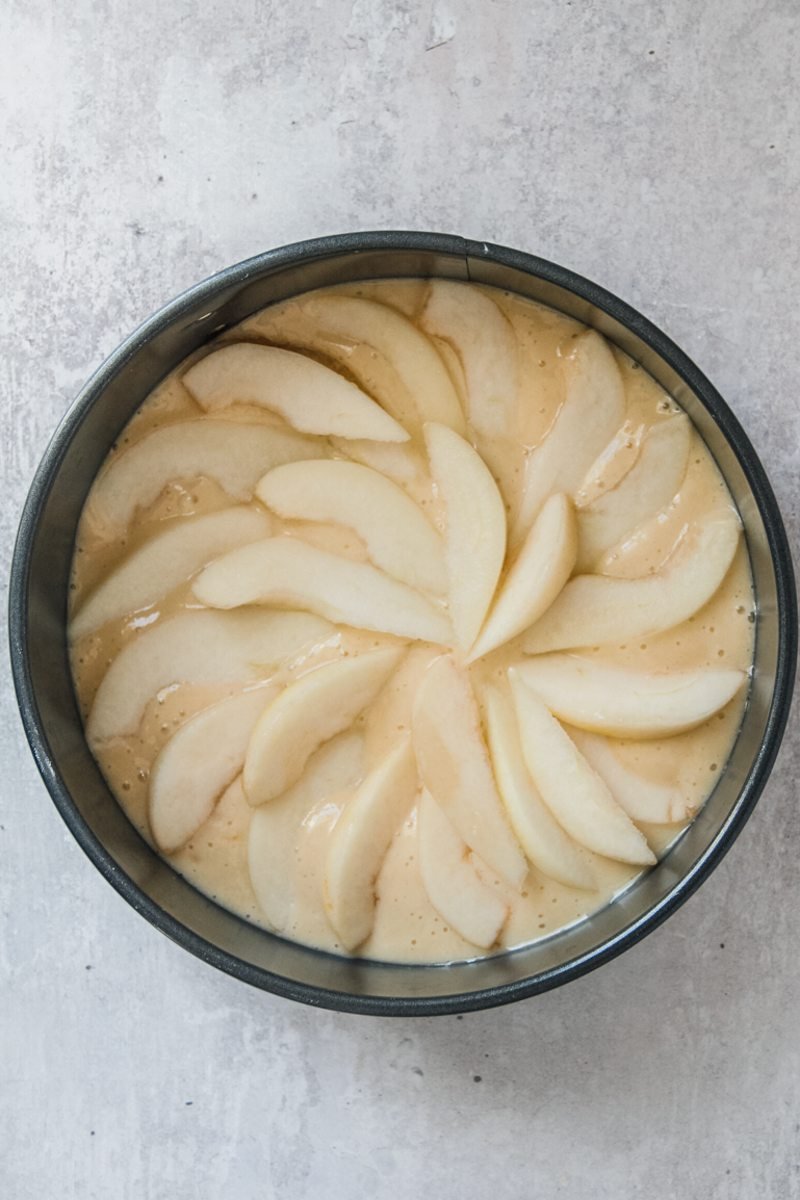 Pear slices sit pressed into a round metal cake tin on a gray surface.