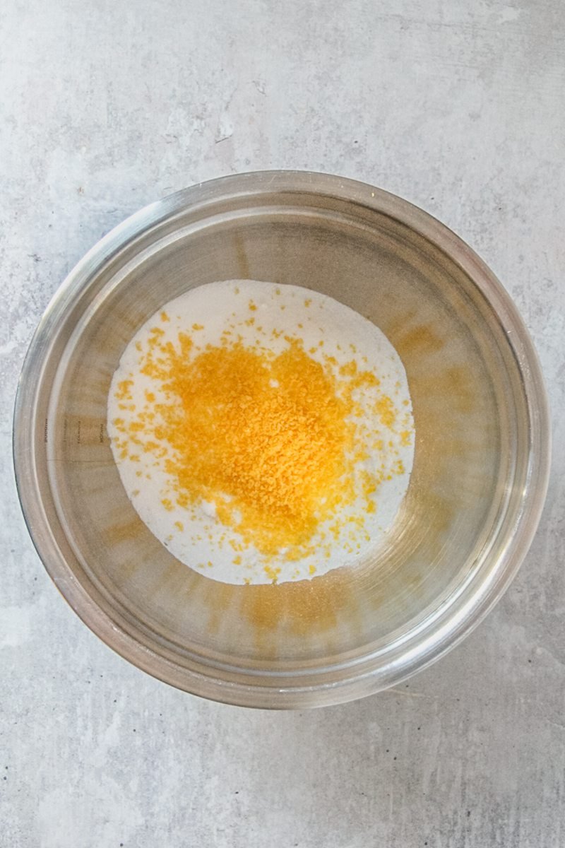 Fine lemon zest and sugar sit in a stainless steel bowl on a gray surface.