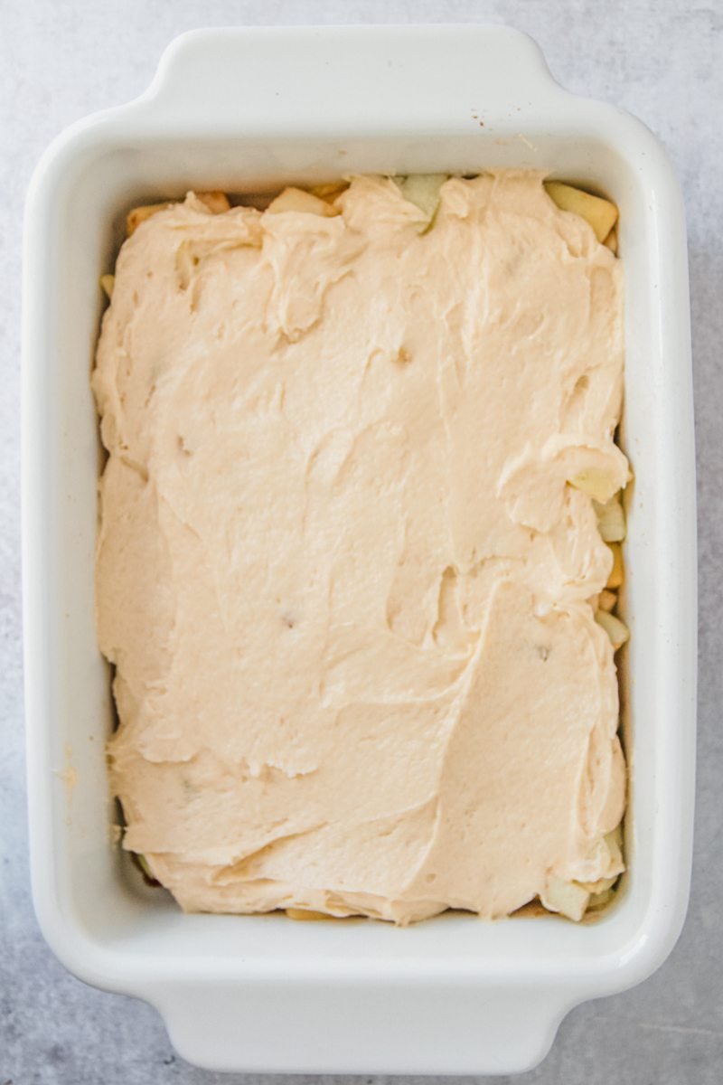 A sponge cake sits on top of apples in a rectangle white baking dish on a gray surface.