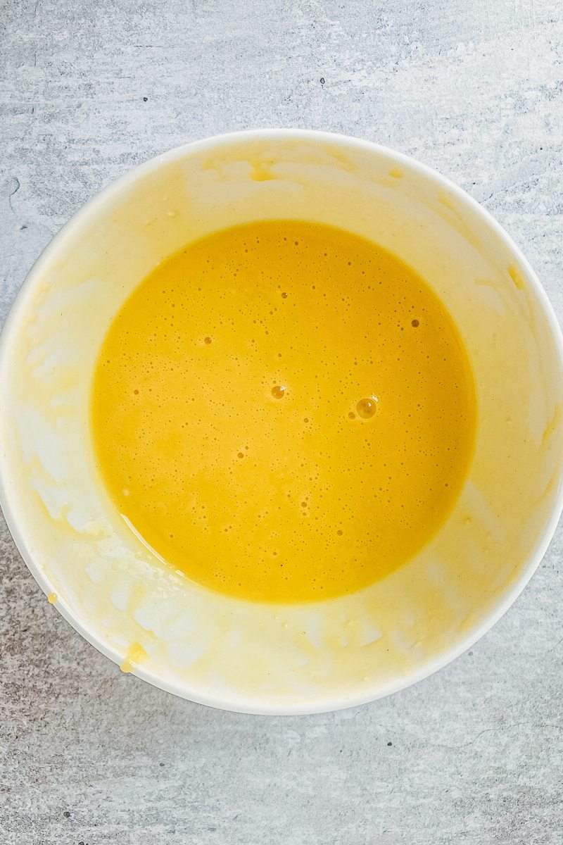 Whisked egg yolks and sugar sit in a white ceramic bowl on a gray surface.