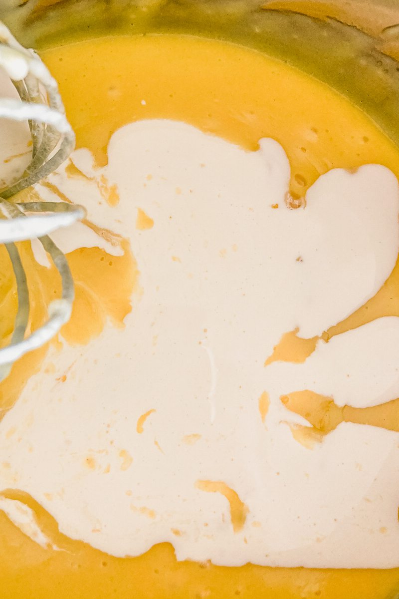 Cream sits on top of a custard in a stainless steel saucepan beside a whisk.