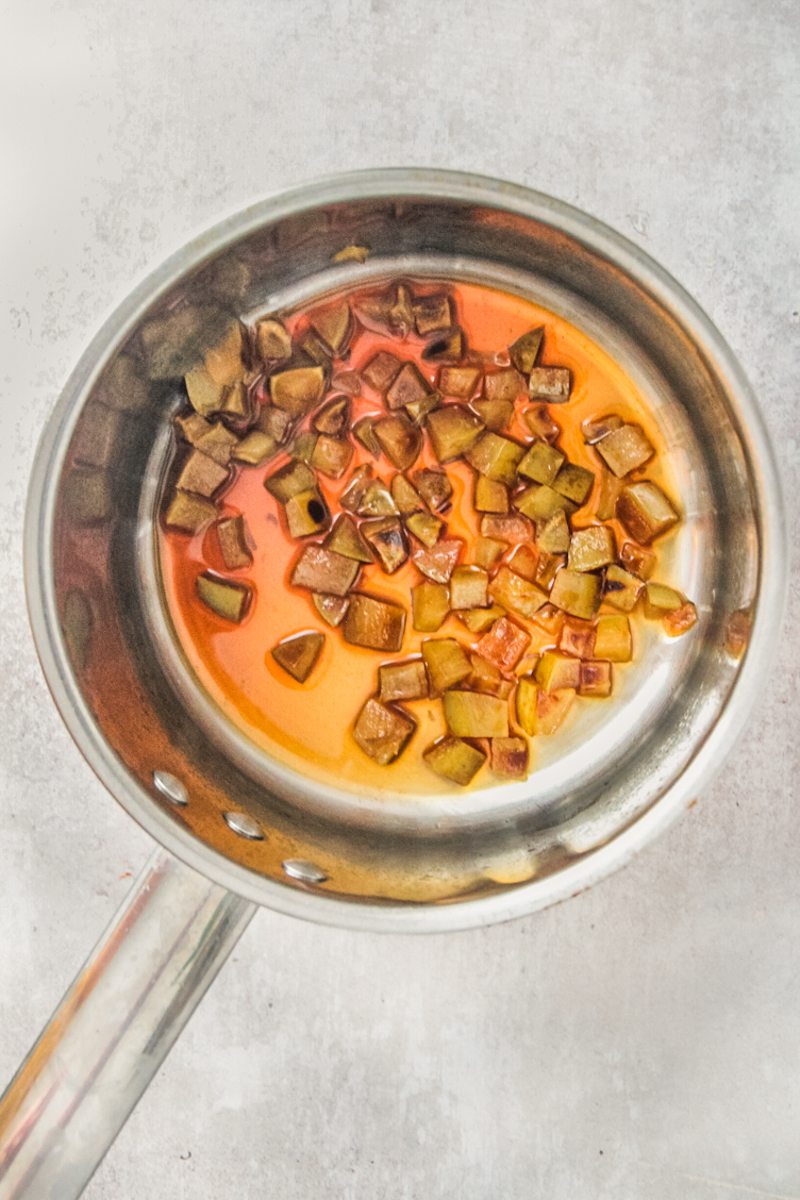 Caramelized apple cubes sit in a stainless steel saucepan on a gray surface.