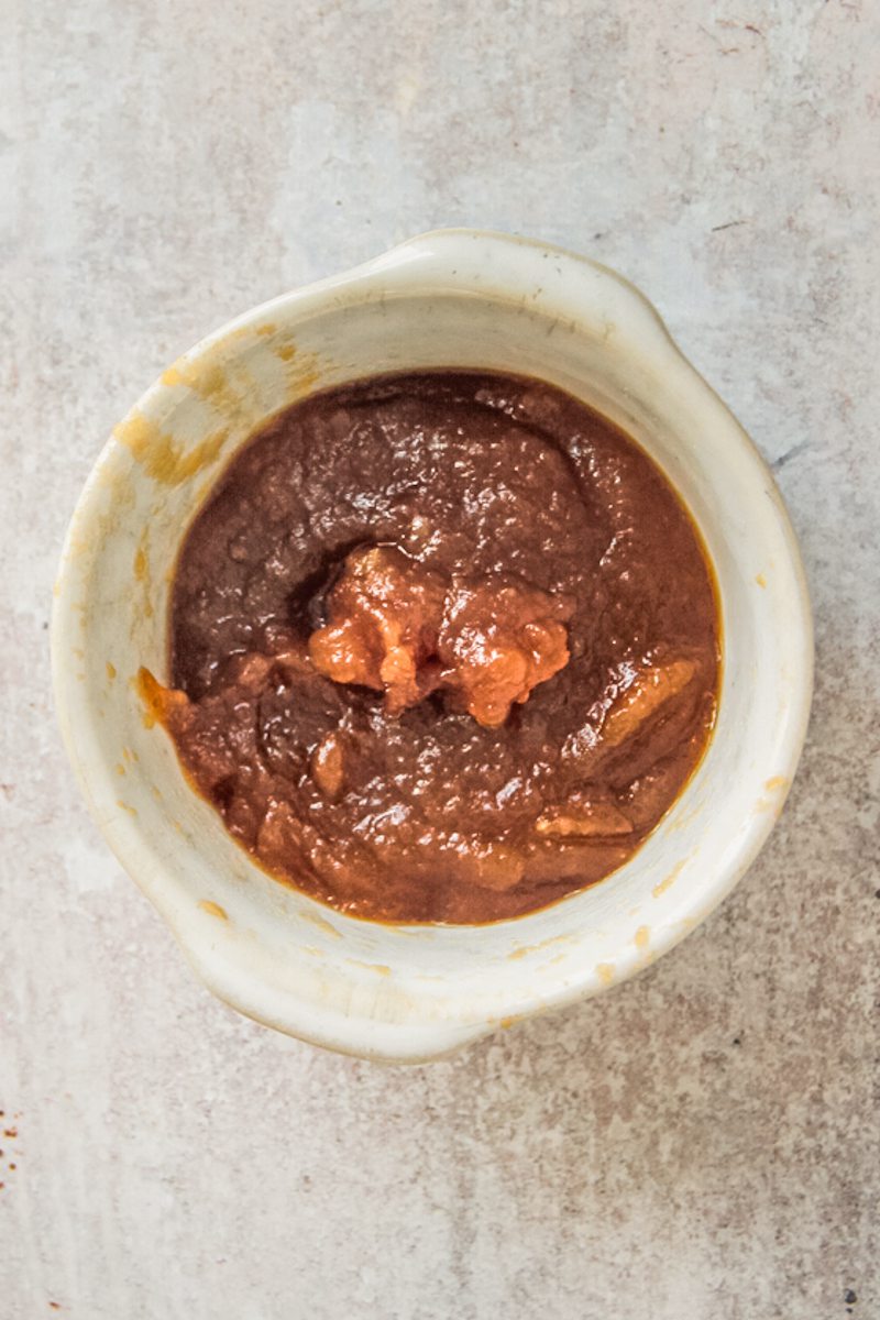 Caramelized apple butter sits in a small ceramic bowl on a gray surface.