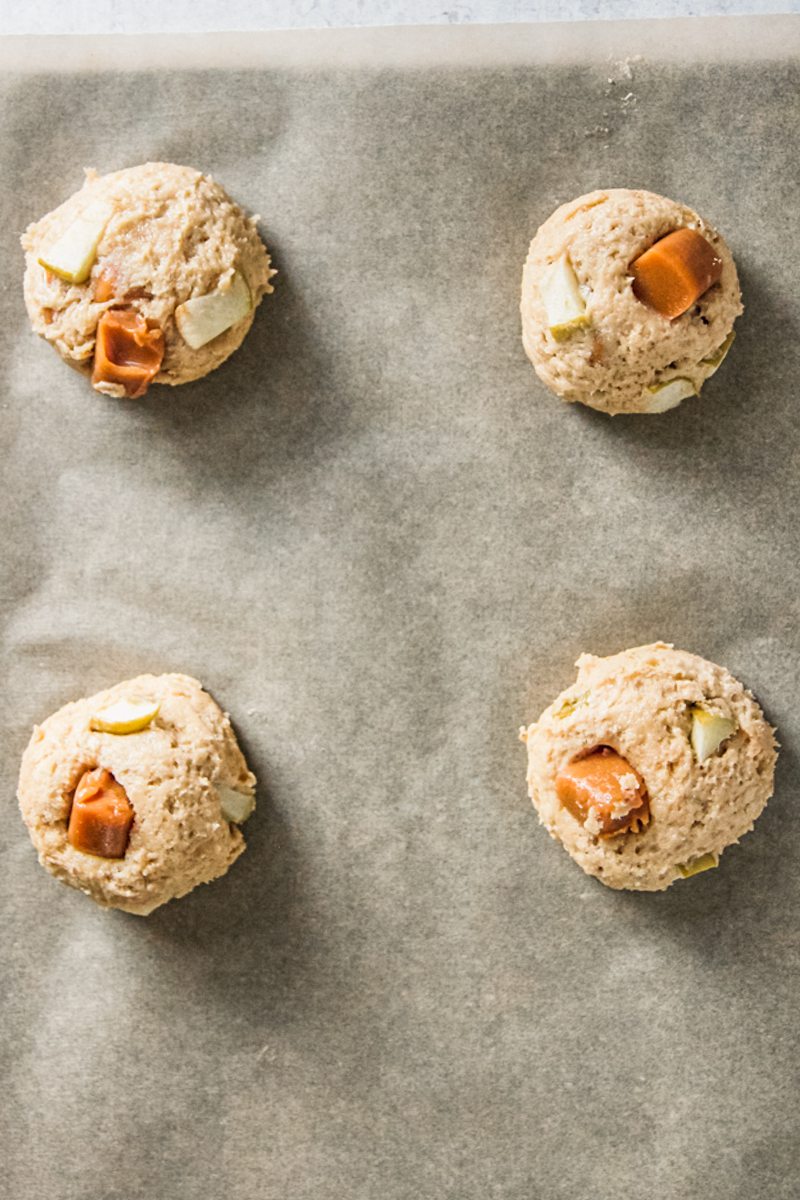 Caramel apple cookie dough balls sit on a lined baking tray.