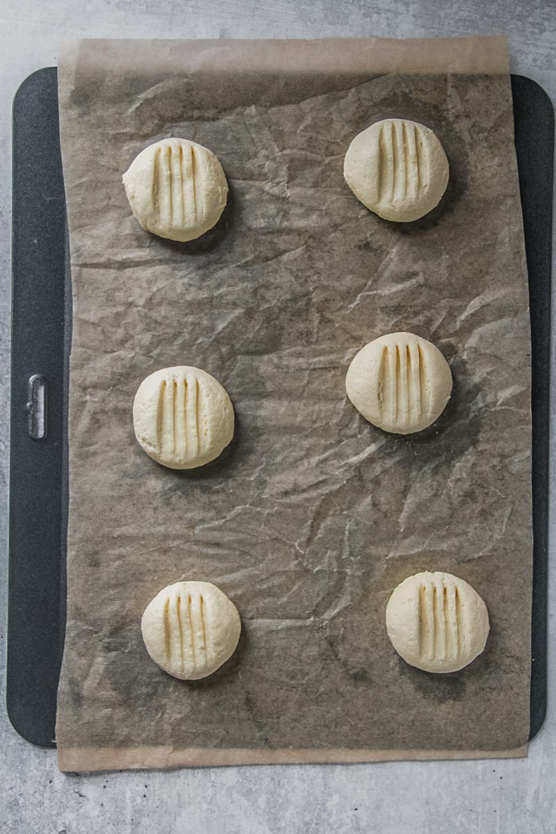 Melting moment biscuits sit on a baking tray on lined with parchment paper on a gray surface.