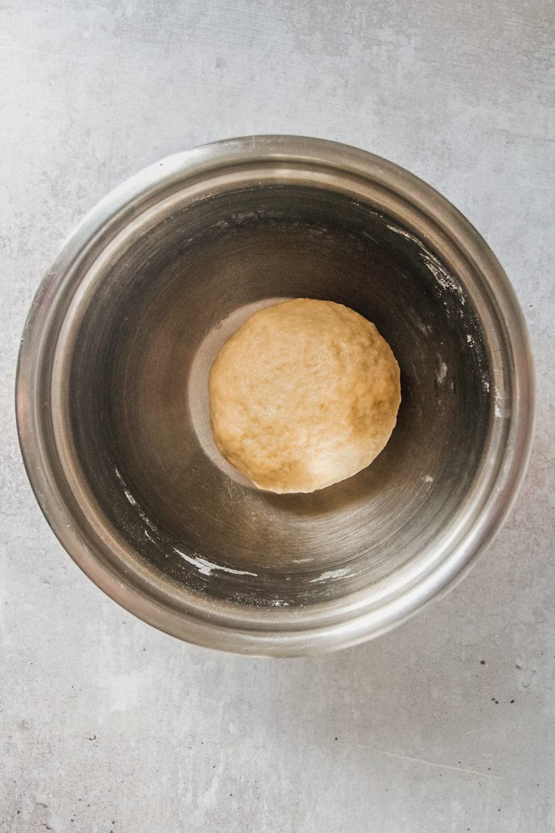 Apple strudel dough sits in a stainless steel bowl on a light gray surface.