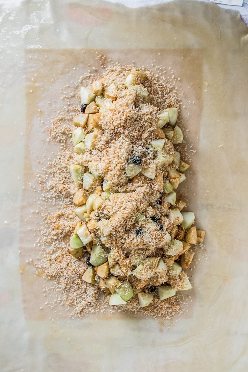 Breadcrumbs sit on top of apples in the center of thin apple strudel pastry.