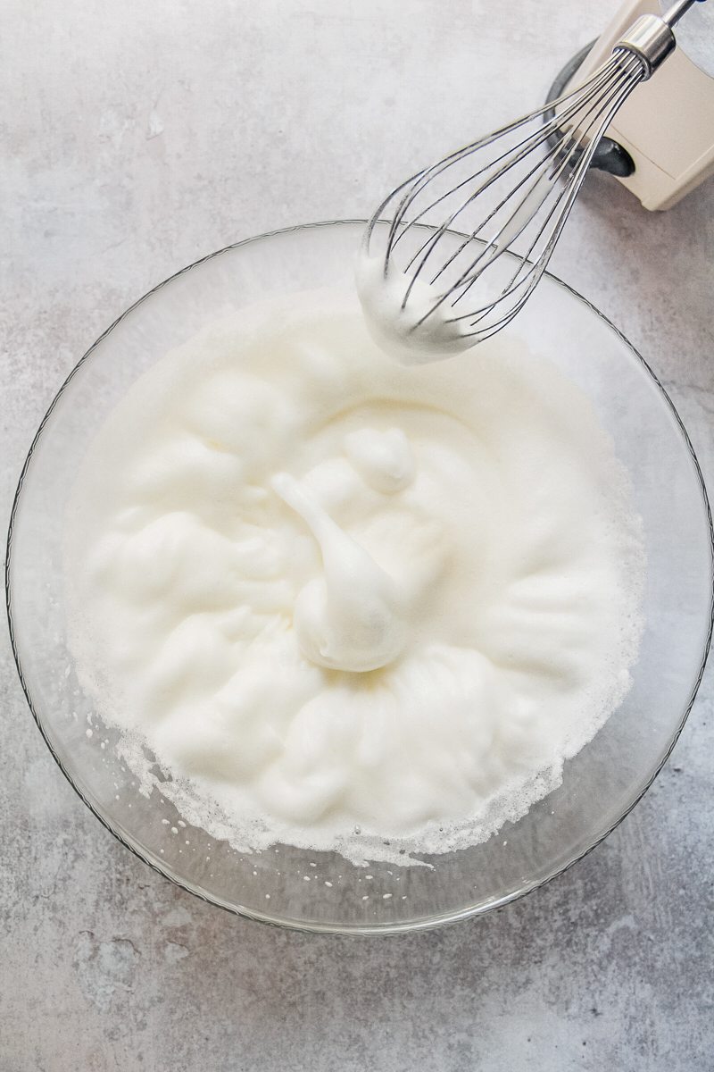 Whipped egg whites sit in a glass bowl on a gray surface.