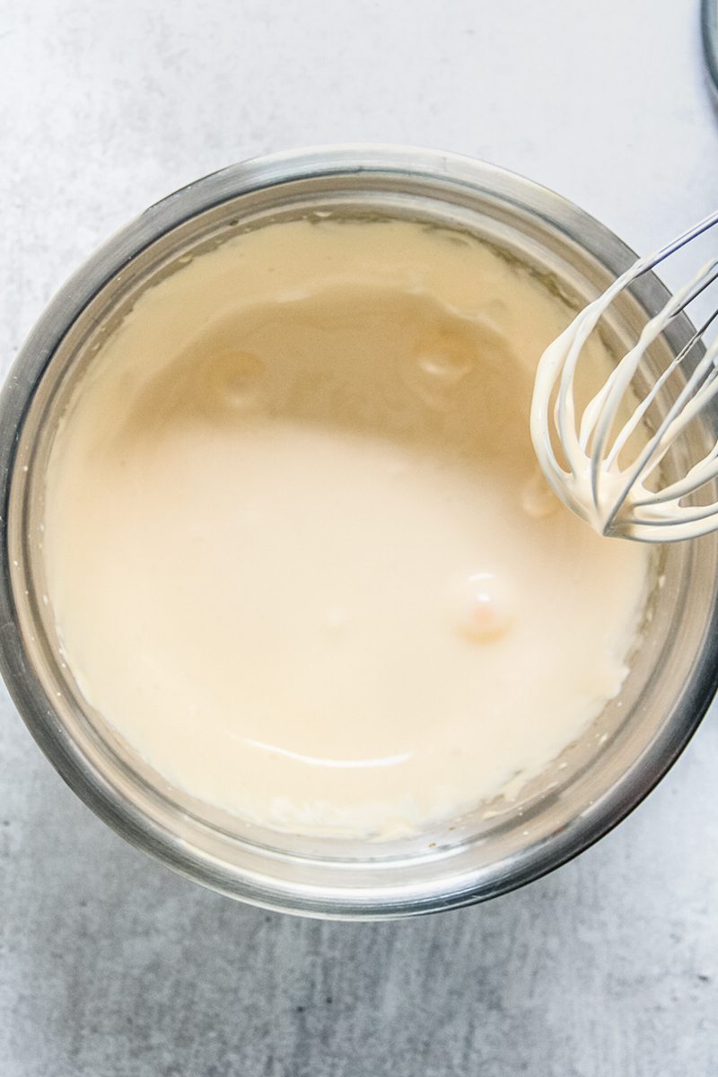 Separately whipped egg yolks and whites that have been combined sit in a stainless steel bowl on a gray surface.