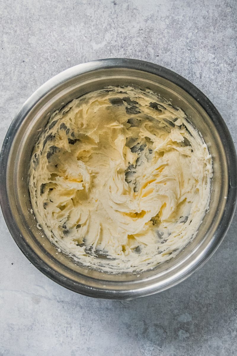 Whipped butter and sugar sits in a stainless steel bowl on a gray surface.