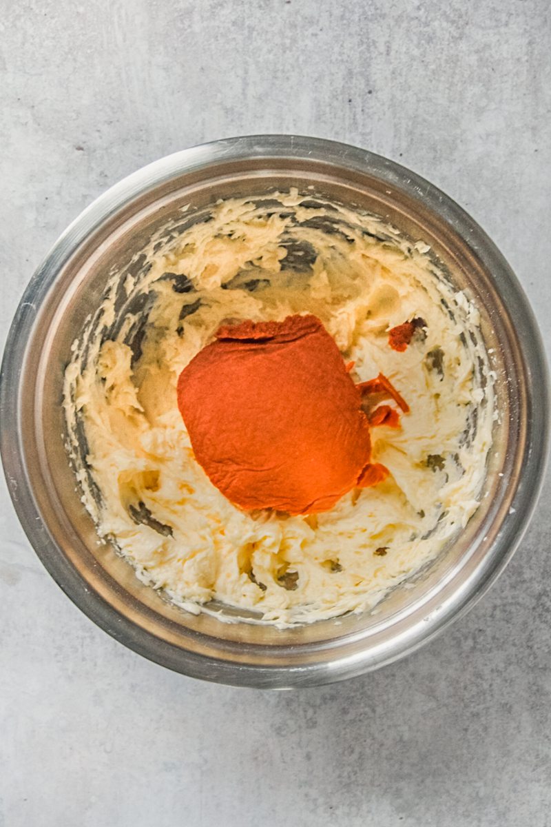 Dried canned pumpkin sits on top of whipped butter and sugar in a stainless steel bowl on a gray surface.